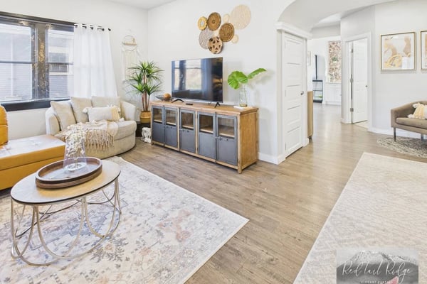 Open-plan living room with cream sofa, TV on wood cabinet, decorative woven baskets on wall, and hardwood floors throughout.