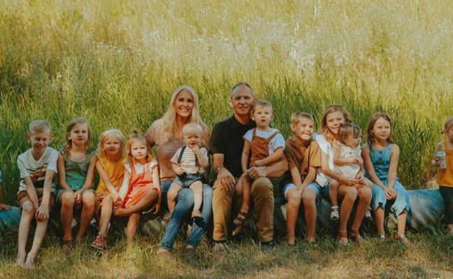 Large family group of adults and children sitting together in front of a tall grain field